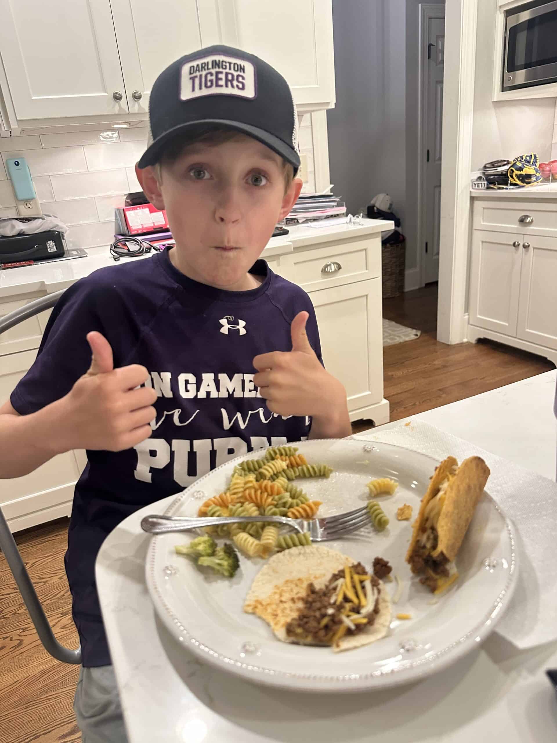 Child enjoying dinner with thumbs up.